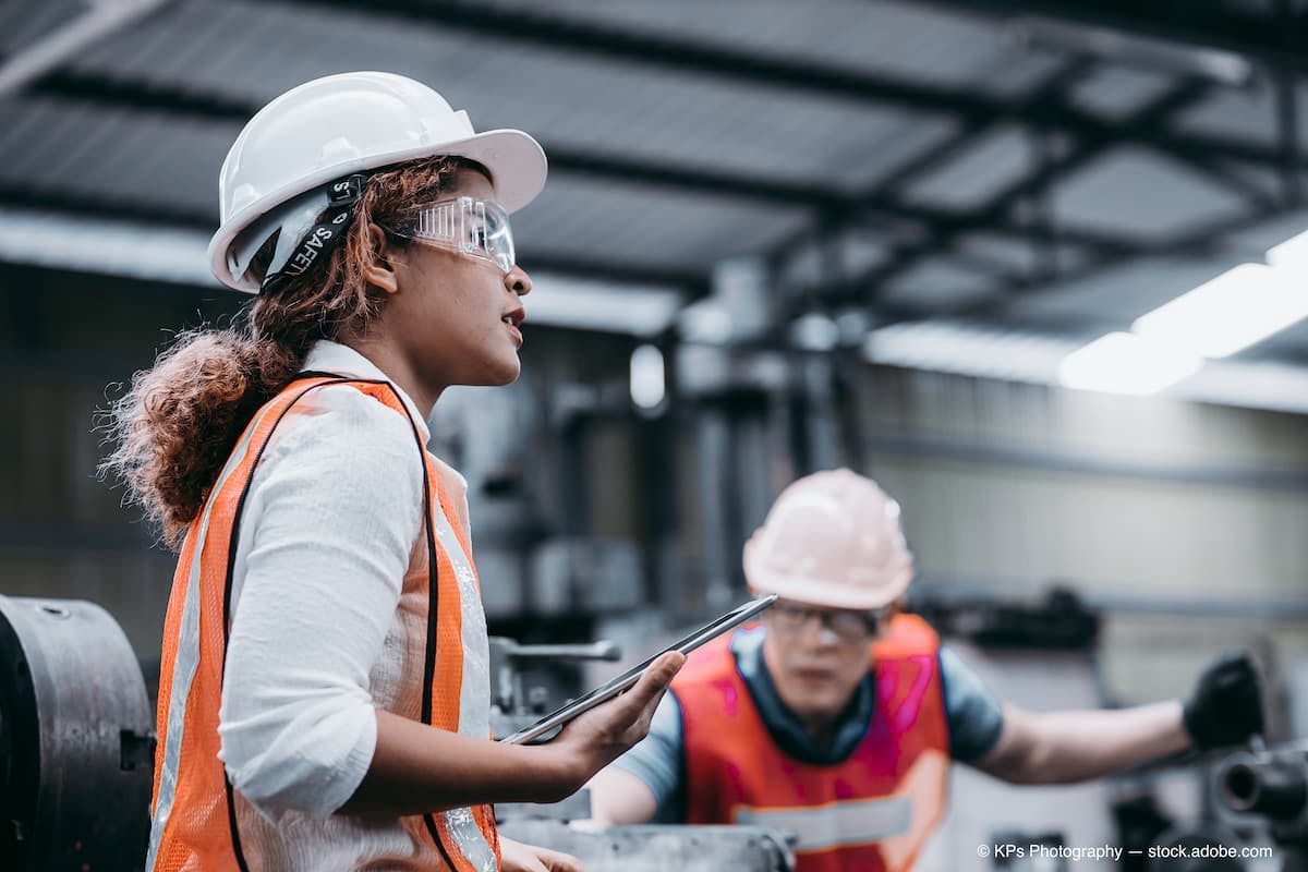 Female industrial engineer wearing a white helmet while standing in a heavy industrial factory behind she talking with workers, Various metal parts of the project (Adobe Stock / KPs Photography)