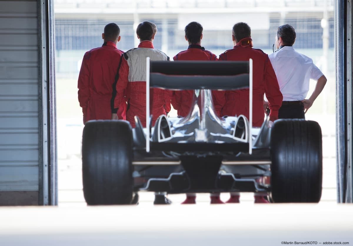 Pit crew standing in front of F1 car Image Credit: AdobeStock/MartinBarraud/KOTO