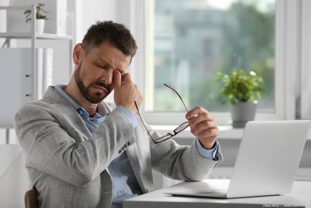 Man rubbing eyes at desk with laptop Image credit: ©New Africa - adobe.stock.com