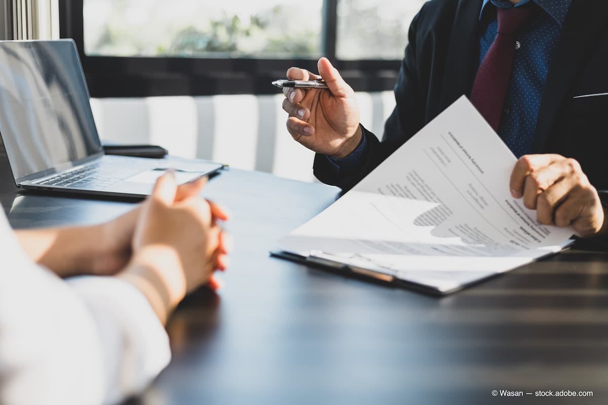 Stock image of a business agreement, with one person signing a contract and another person sitting across the table from them. (Adobe Stock / Wasan)