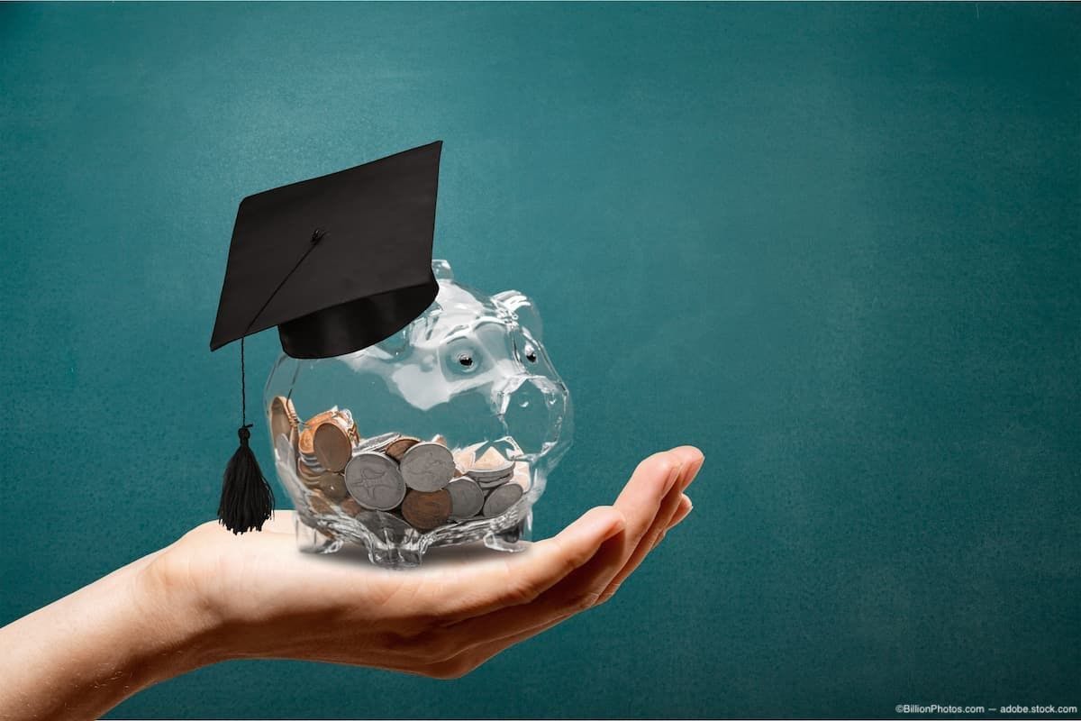 Hand holding a clear piggy bank with coins inside and wearing a grad cap Image Credit: AdobeStock/BillionPhotos.com