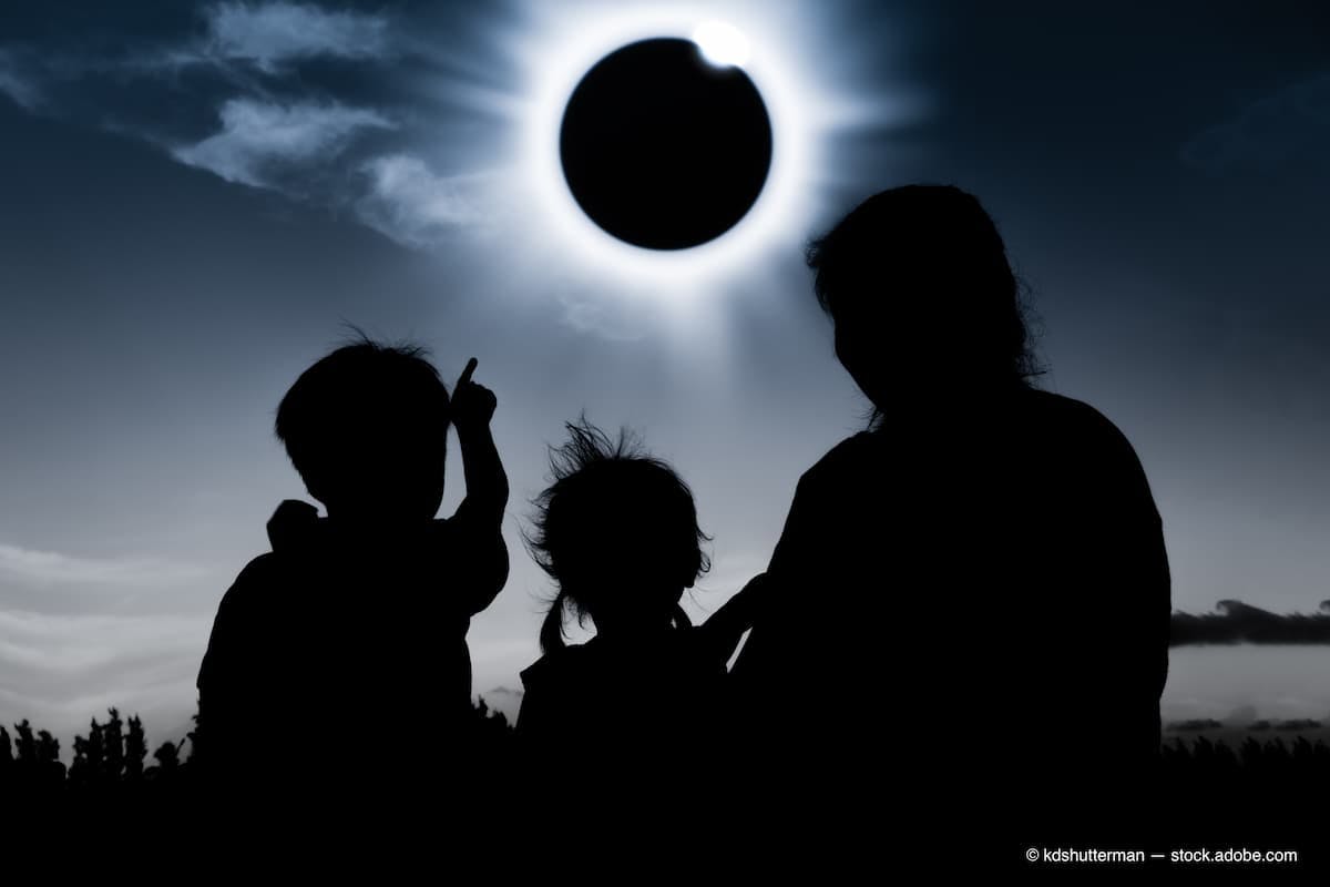 Silhouette back view of family looking at solar eclipse on dark sky (Adobe Stock / kdshutterman)
