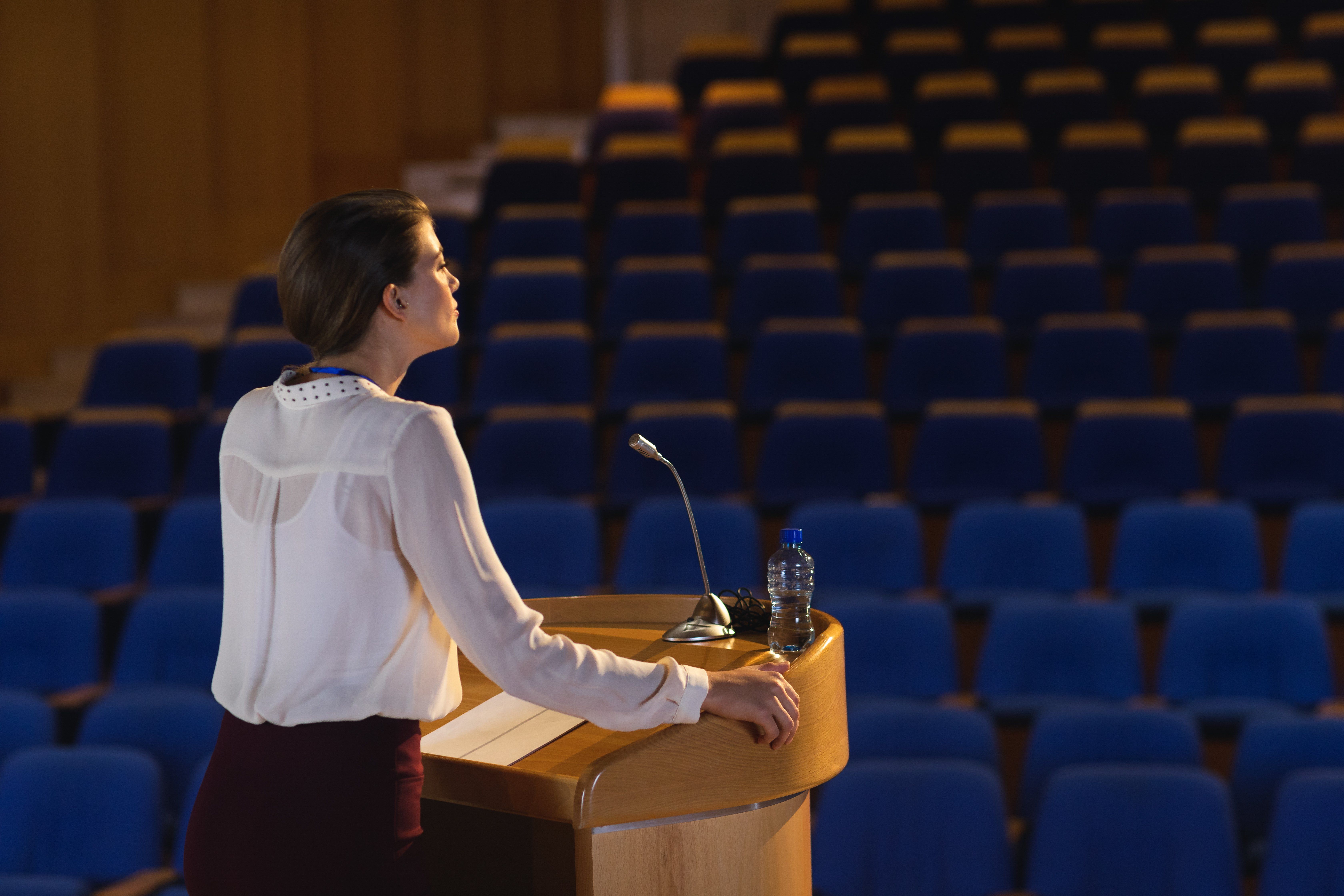 a woman stands at a podium in front of empty seats